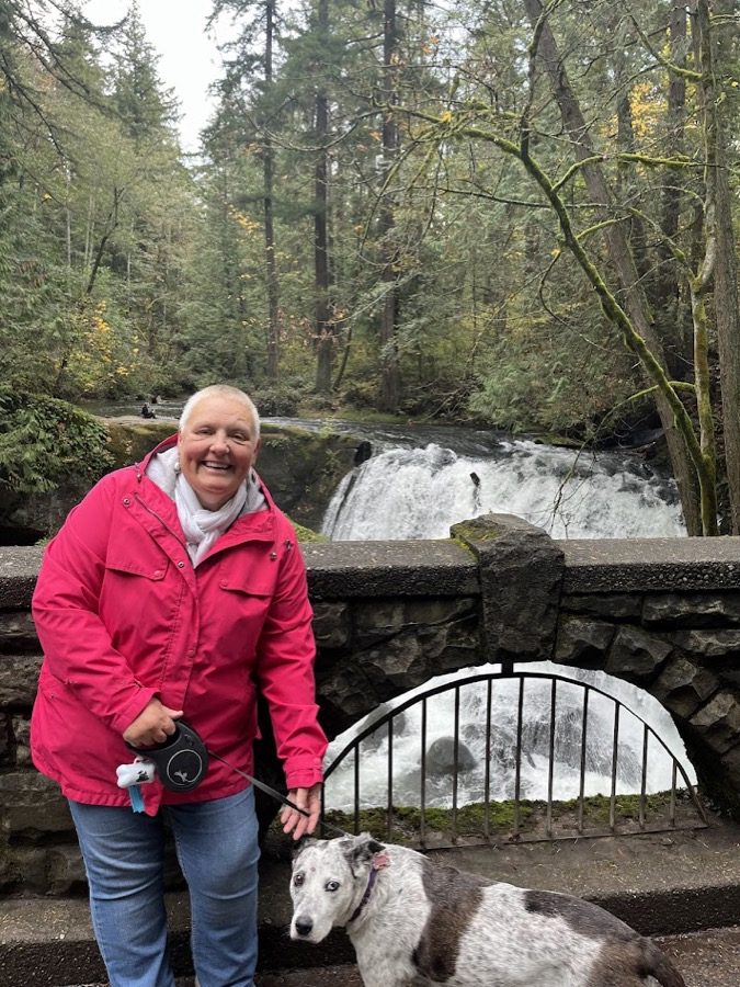 Michelle in a red coat beside a grey dog at a waterfall in Washington State