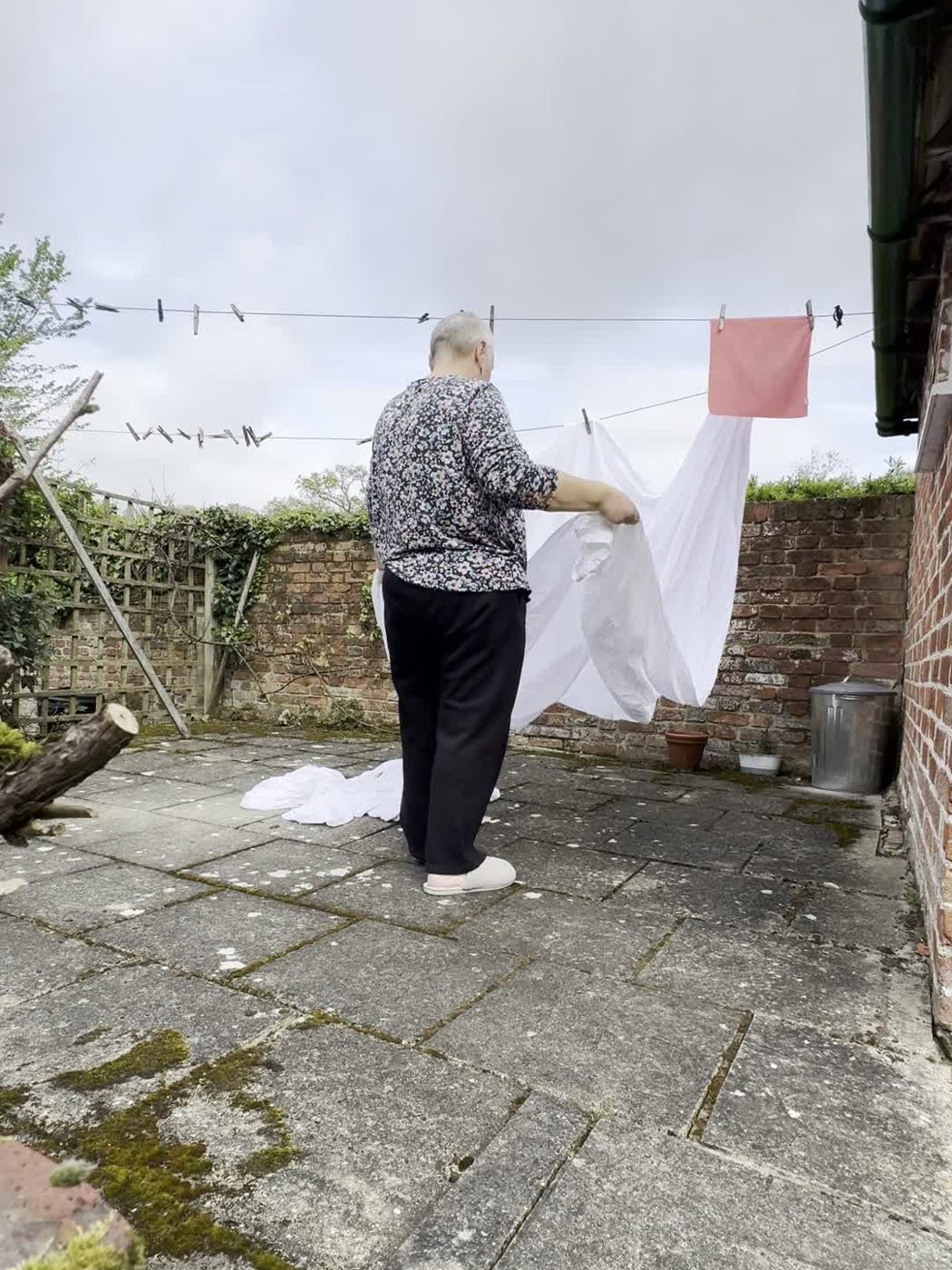 Michelle pegging white sheets on a washing line in a walled garden at Wye